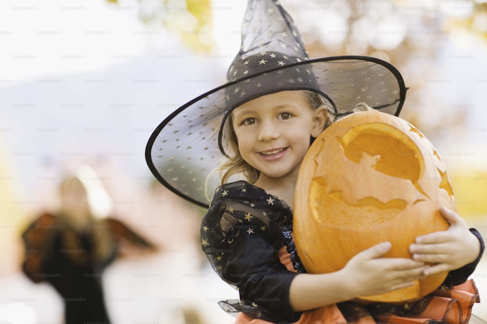 a little girl in a witch costume holding a pumpkin