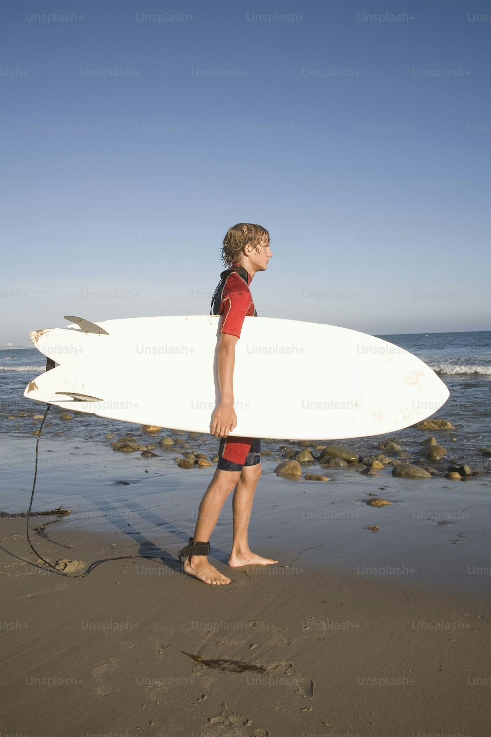 a young boy holding a white surfboard on top of a sandy beach