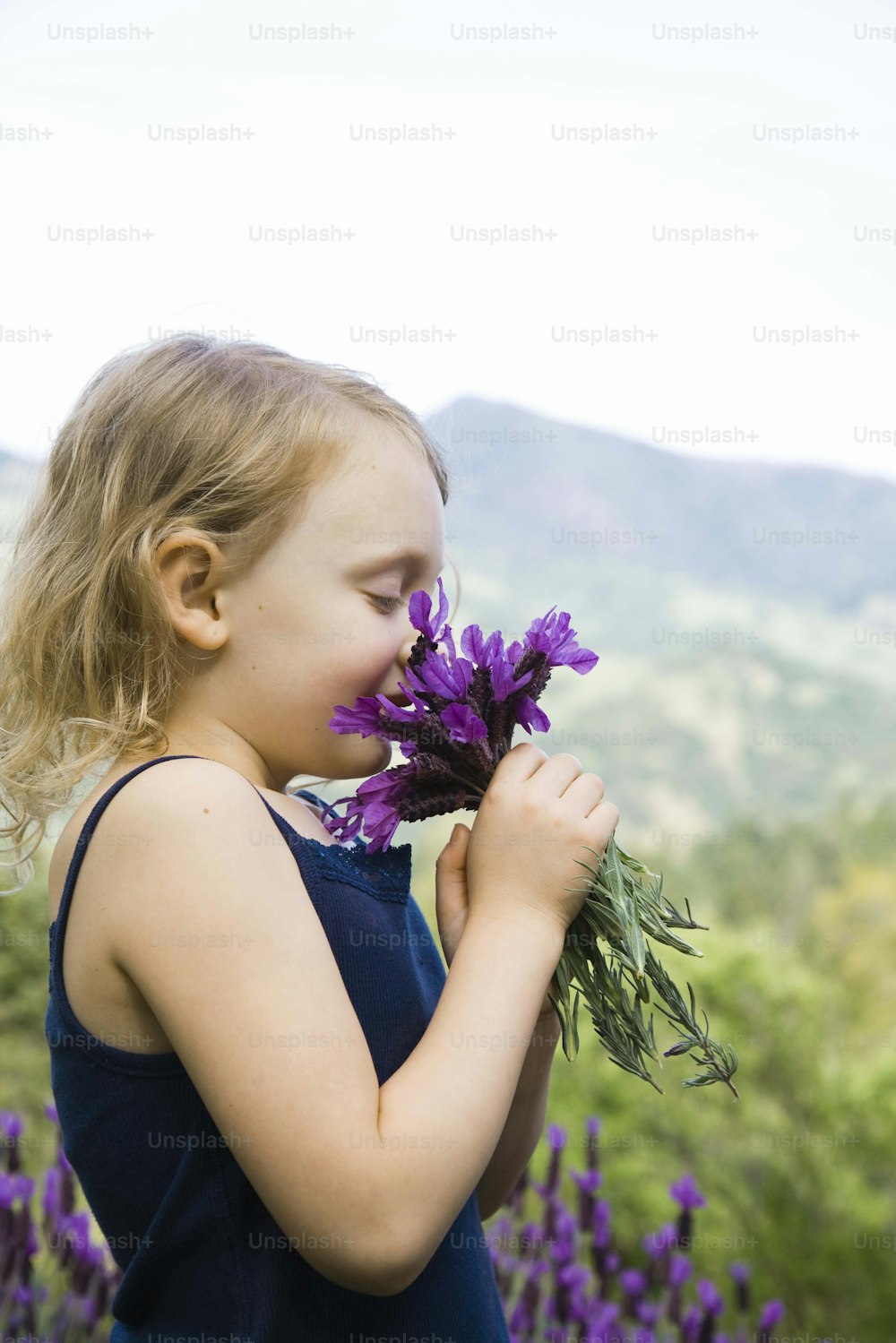 a little girl smelling a bunch of purple flowers