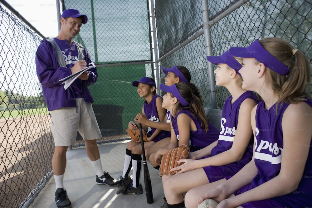 a group of young girls sitting next to each other on a baseball field