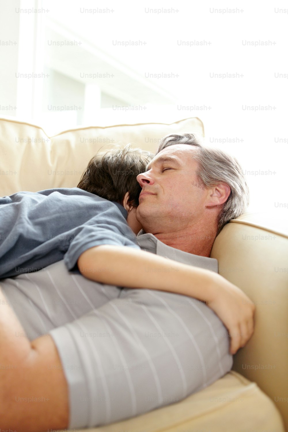 A father and son sleeping together on the lounge sofa after an active day