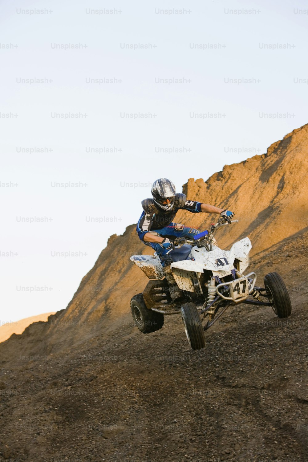 um homem montado em um veículo branco de quatro rodas no topo de uma colina de terra
