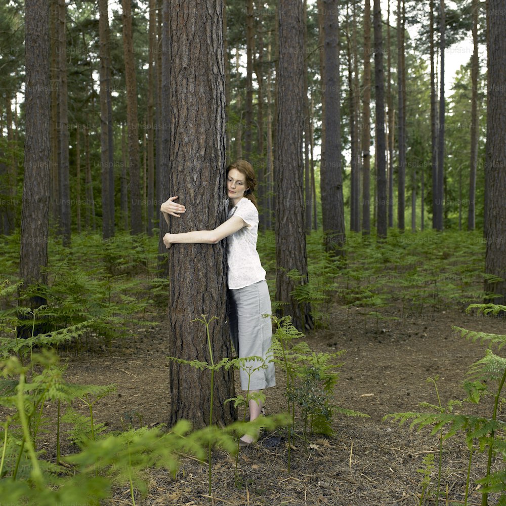 a woman standing next to a tree in a forest