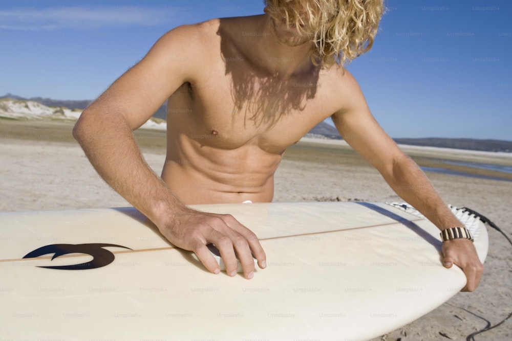 a shirtless man holding a surfboard on the beach