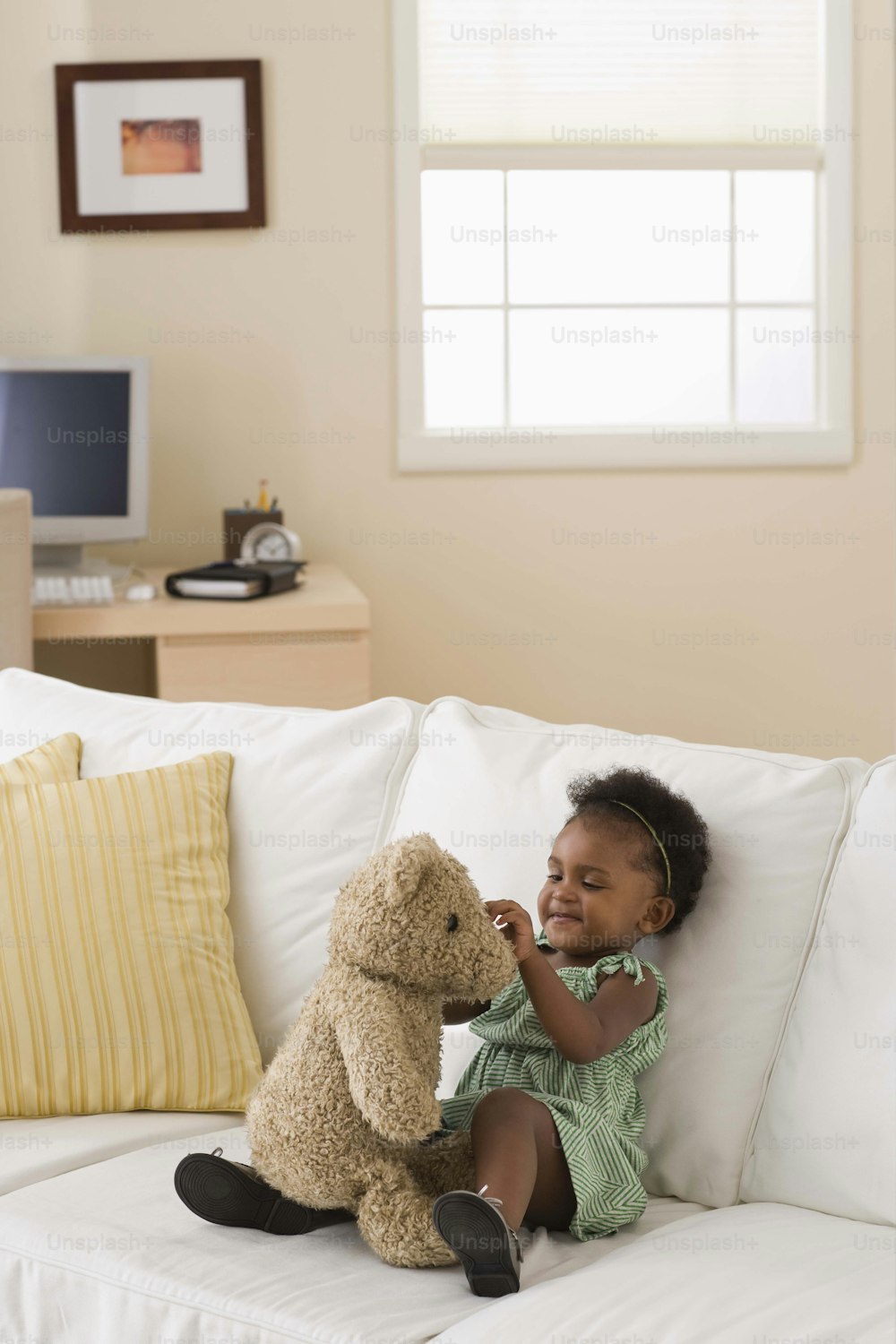 Ein kleines Mädchen, das mit einem Teddybären auf einer Couch sitzt