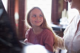 a little girl sitting next to a woman at a piano