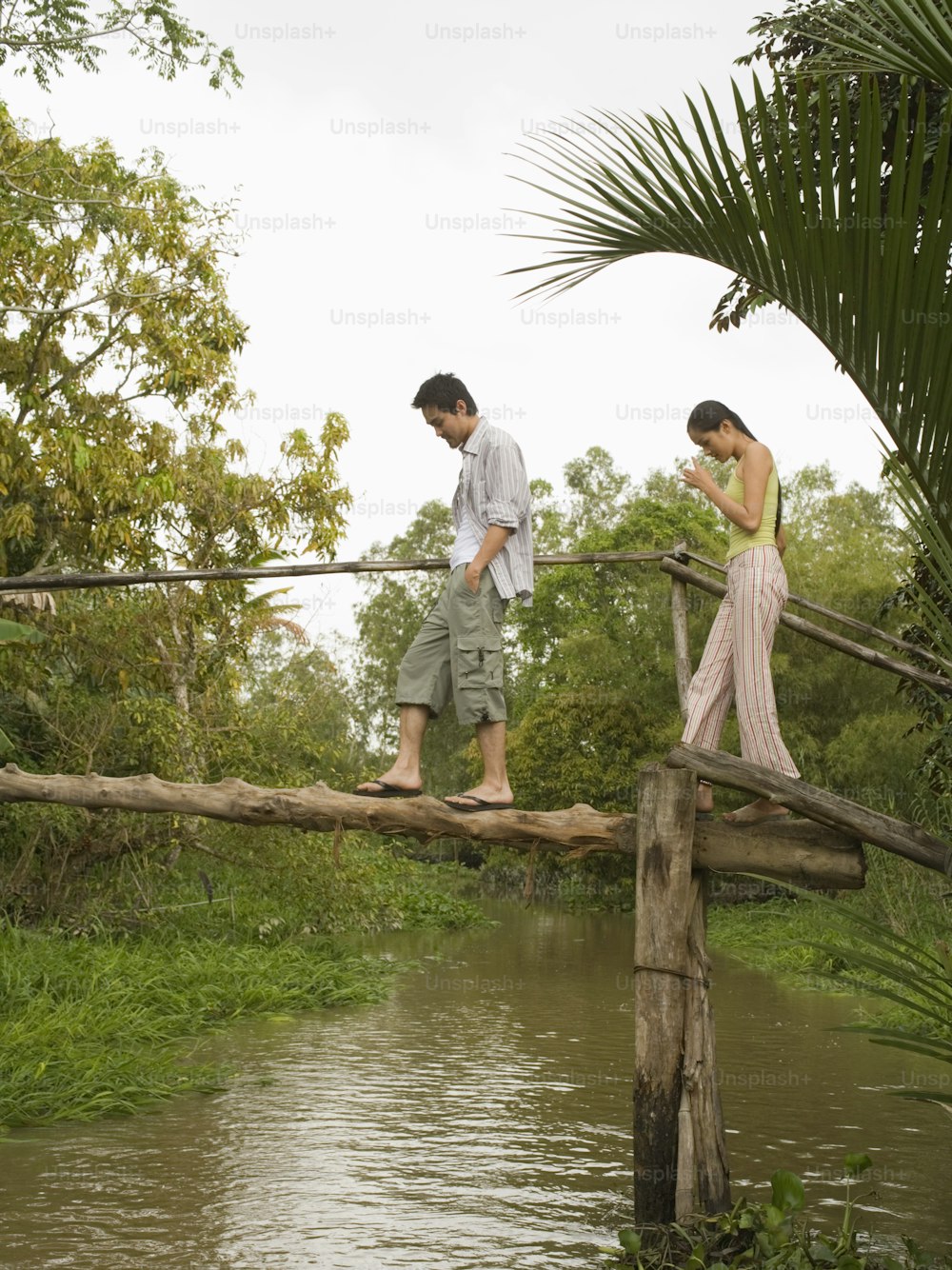 a man and woman walking across a wooden bridge over a river