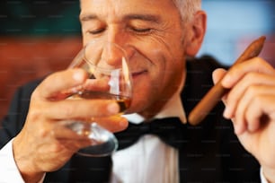 a man in a tuxedo drinking a glass of wine