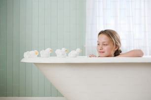 a little girl sitting in a bathtub with ducks