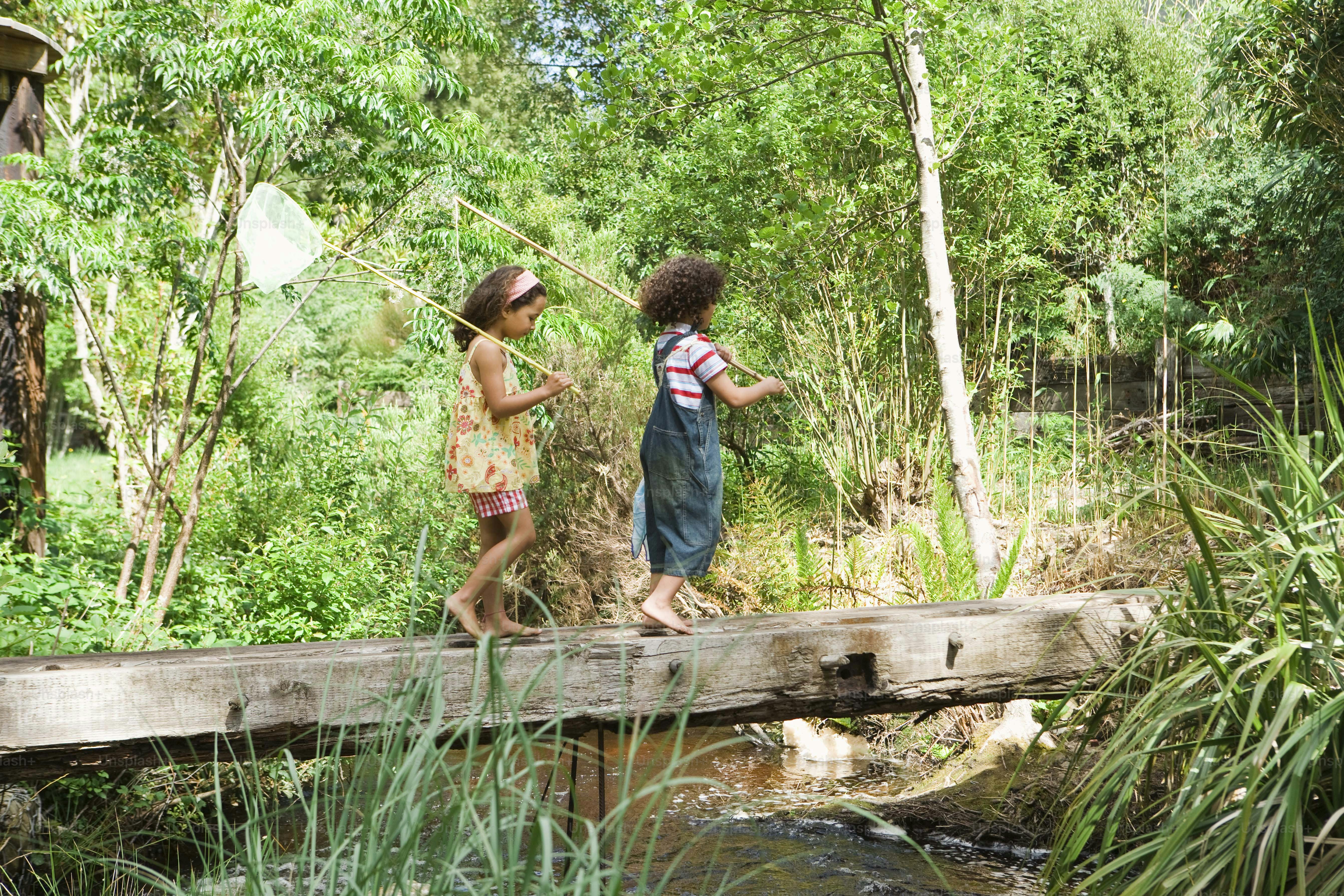 a couple of kids walking across a wooden bridge