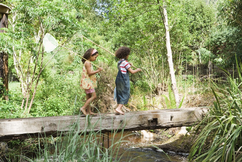 a couple of kids walking across a wooden bridge