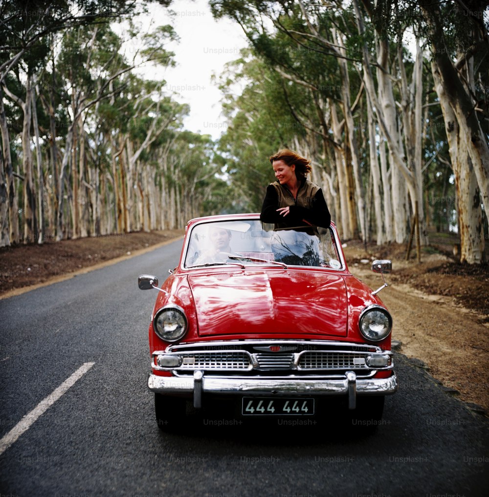a woman sitting in a red car on the side of the road