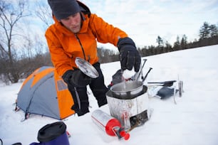 a man in an orange jacket preparing food in the snow