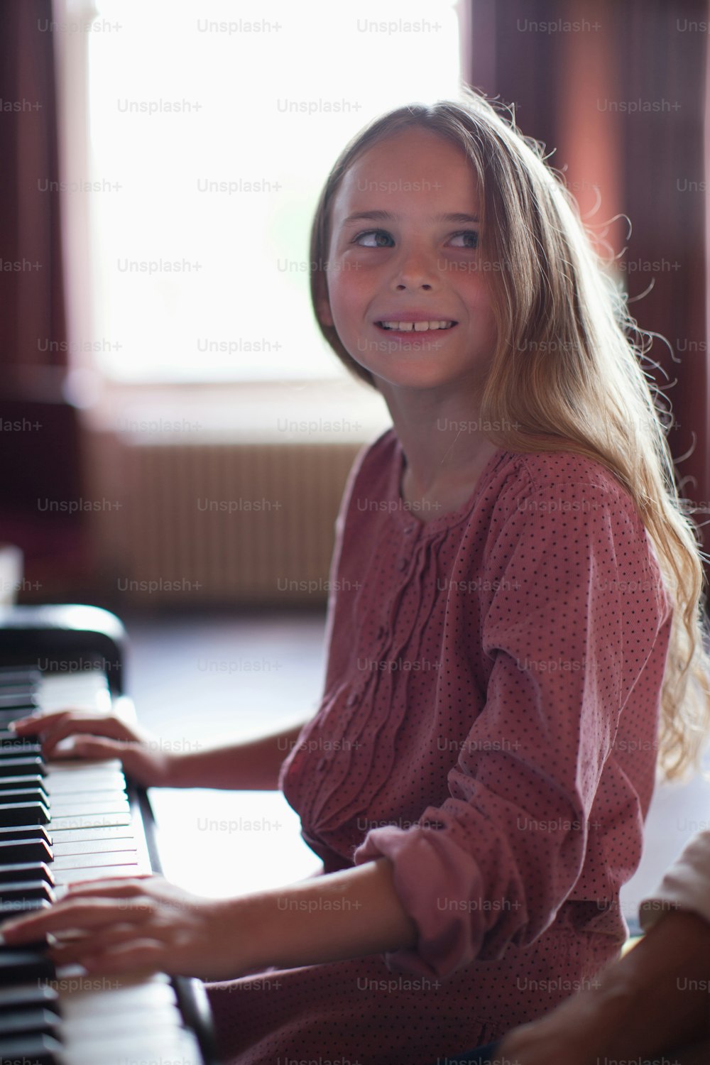 a young girl sitting at a piano smiling
