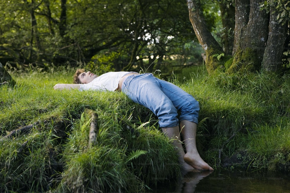 Una persona acostada en la hierba junto a un cuerpo de agua