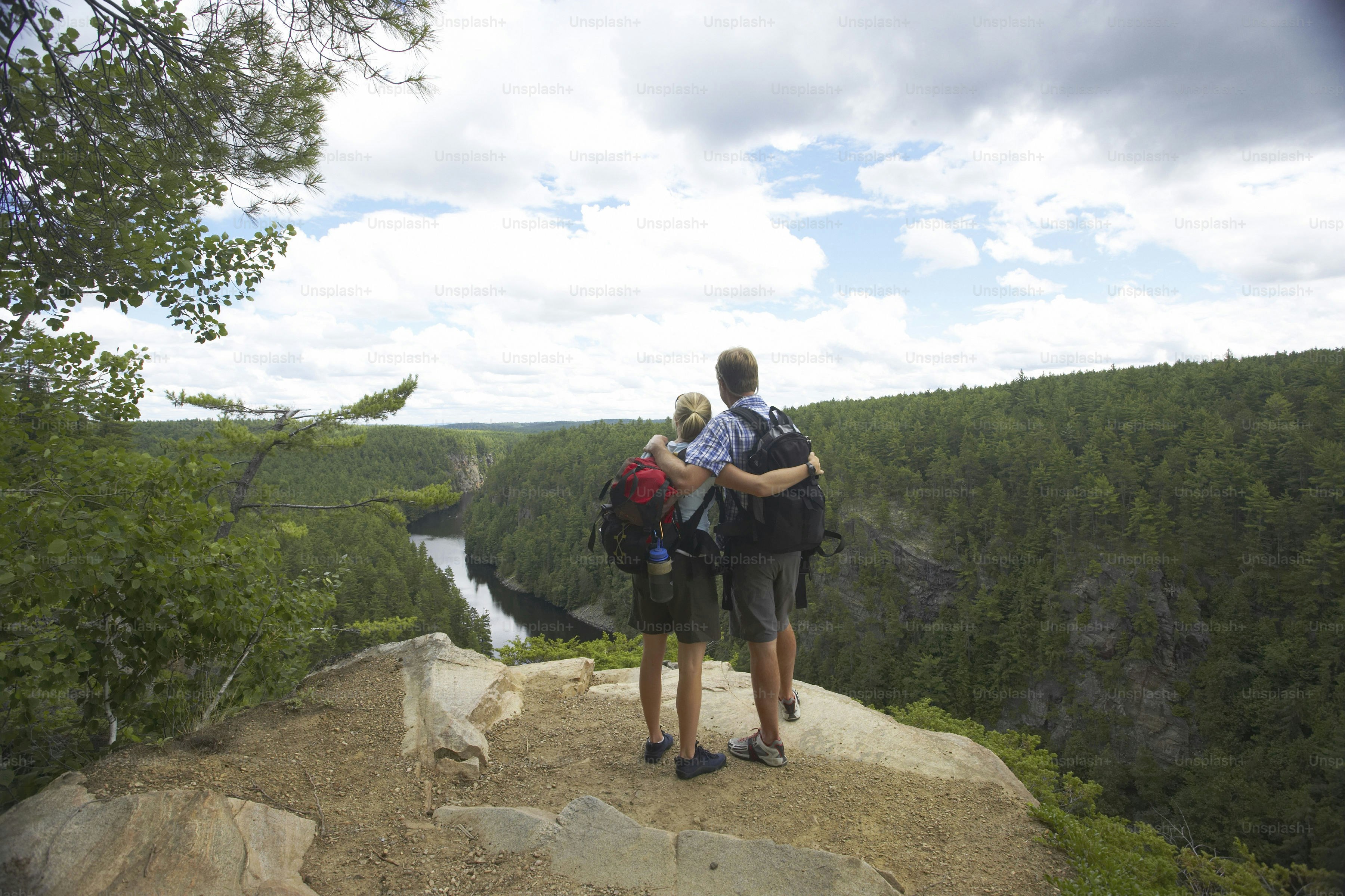 A couple of people standing on top of a cliff photo – River Image on ...