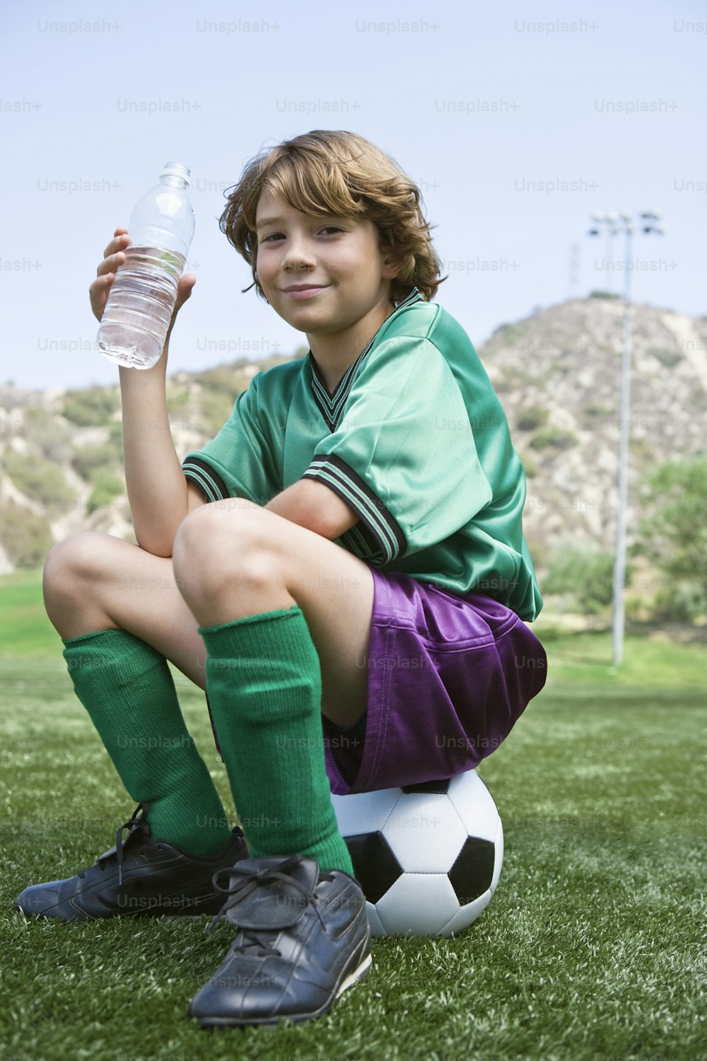 a young boy sitting on top of a soccer ball holding a water bottle