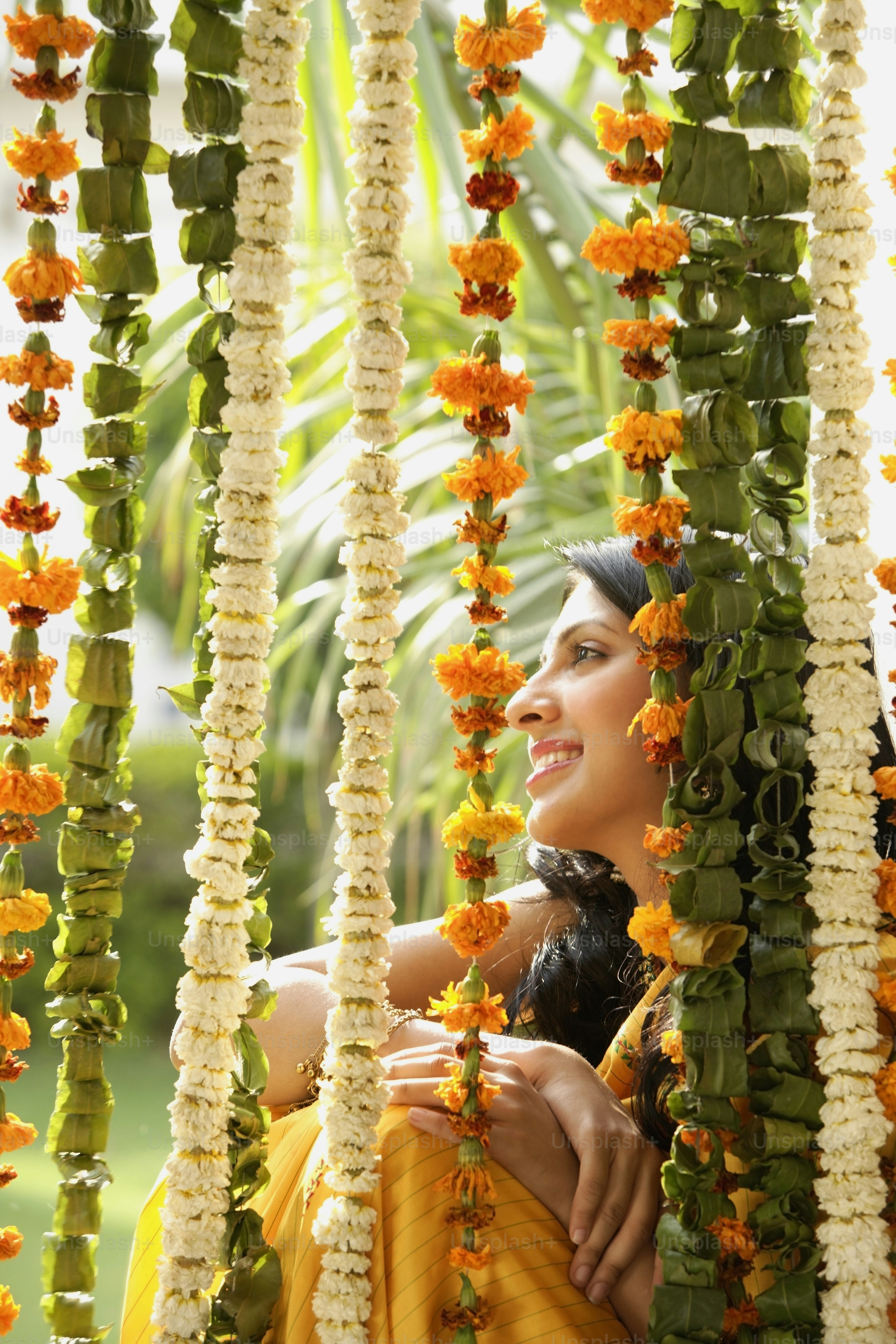 a woman in a yellow sari sitting under a bunch of flowers