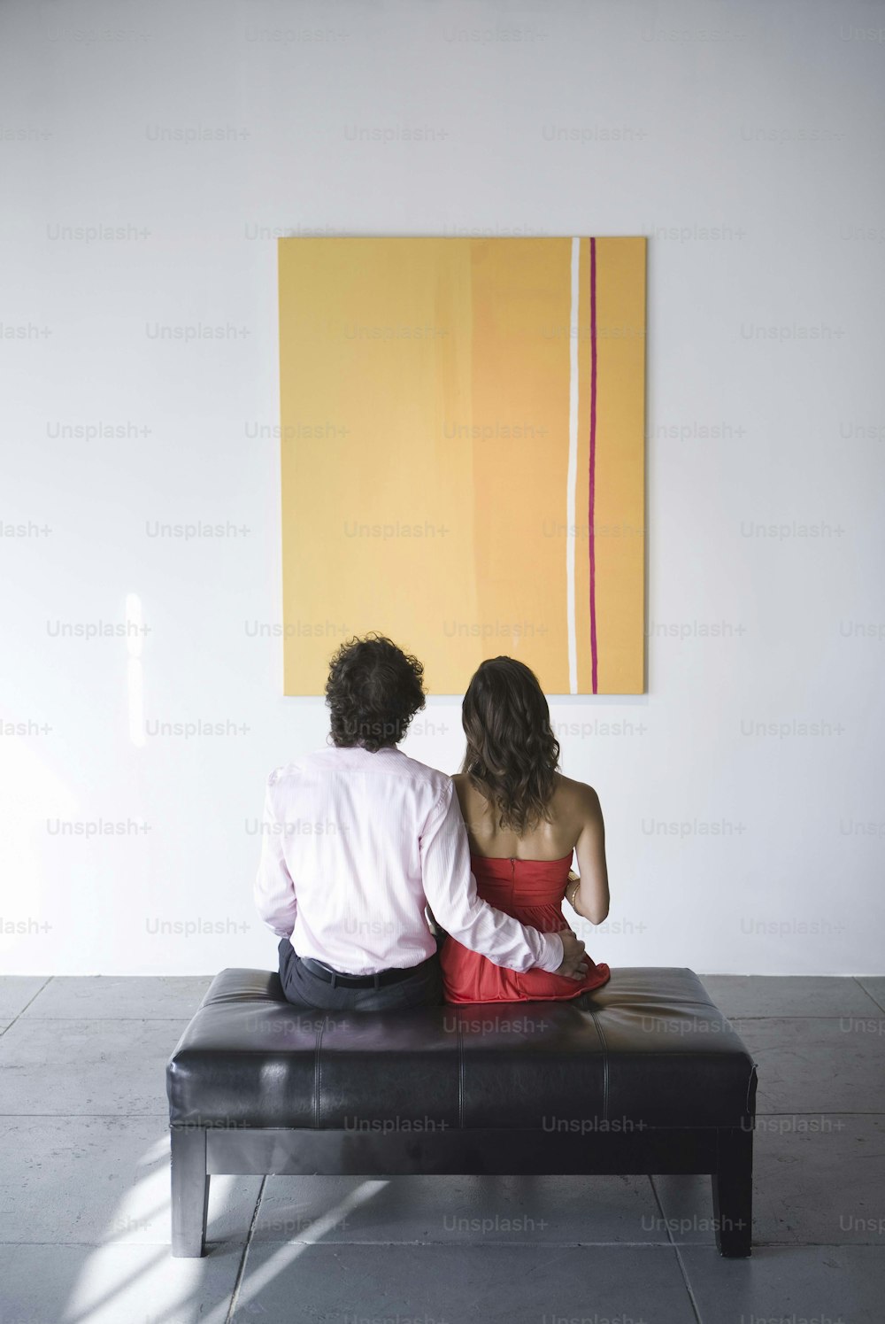 a man and woman sitting on a bench in front of a painting