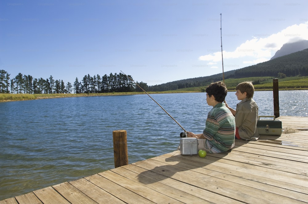 a couple of people sitting on a dock next to a body of water