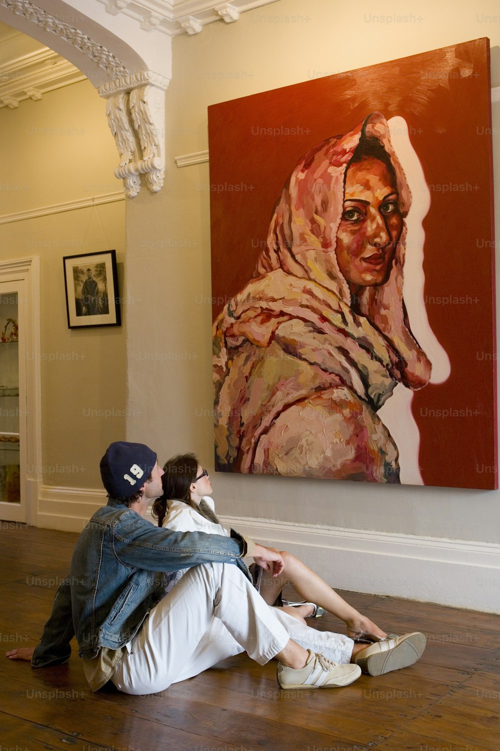 a man and woman sitting on the floor in front of a painting