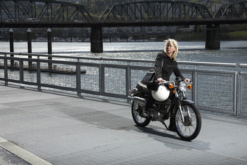 a woman riding a motorcycle across a bridge