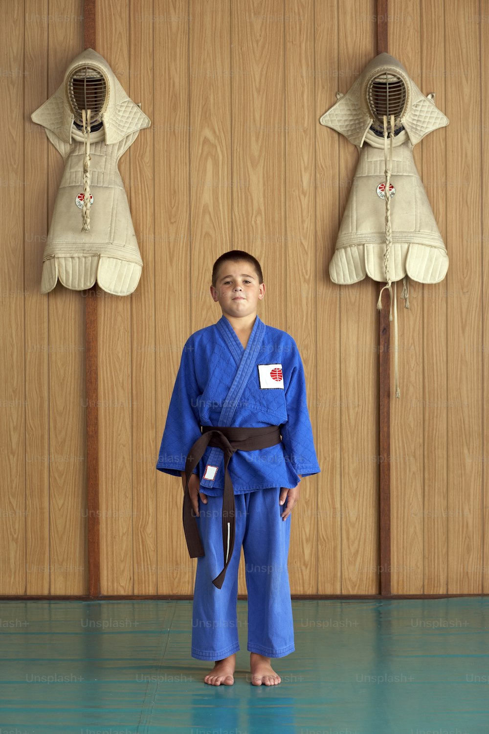 a young boy in a blue kimono standing in front of a wooden wall