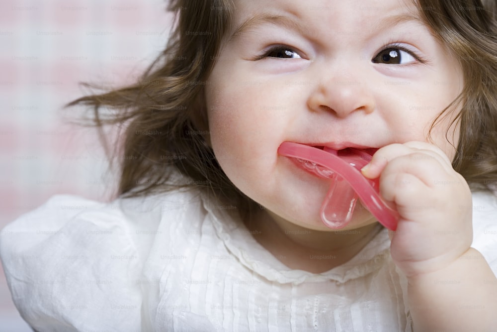 Une petite fille tenant un objet rose dans sa bouche