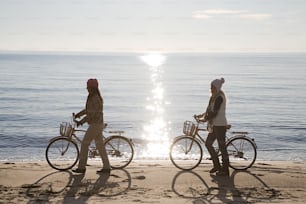 two people walking on the beach with their bikes