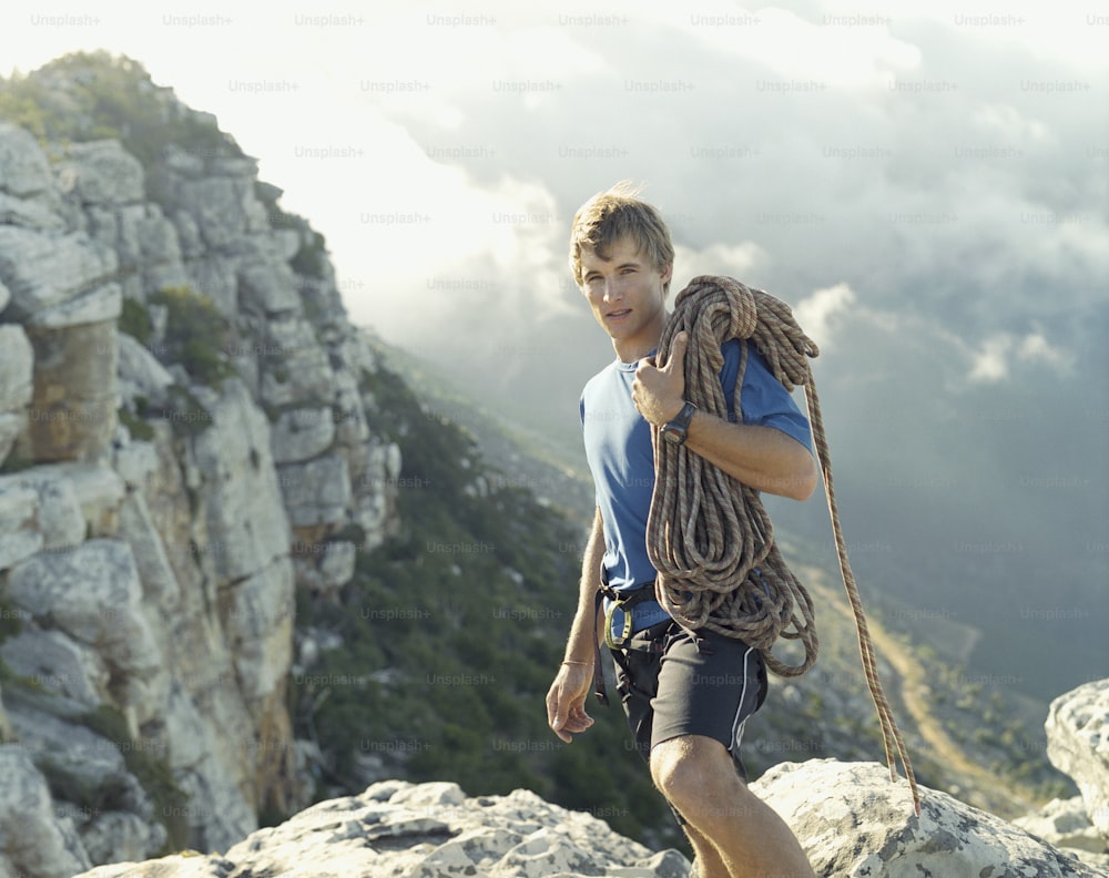 a man with a rope on his back walking up a mountain