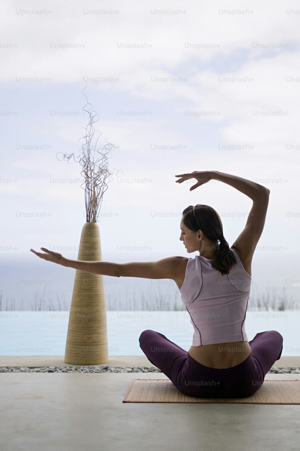 a woman sitting on a yoga mat in front of a vase