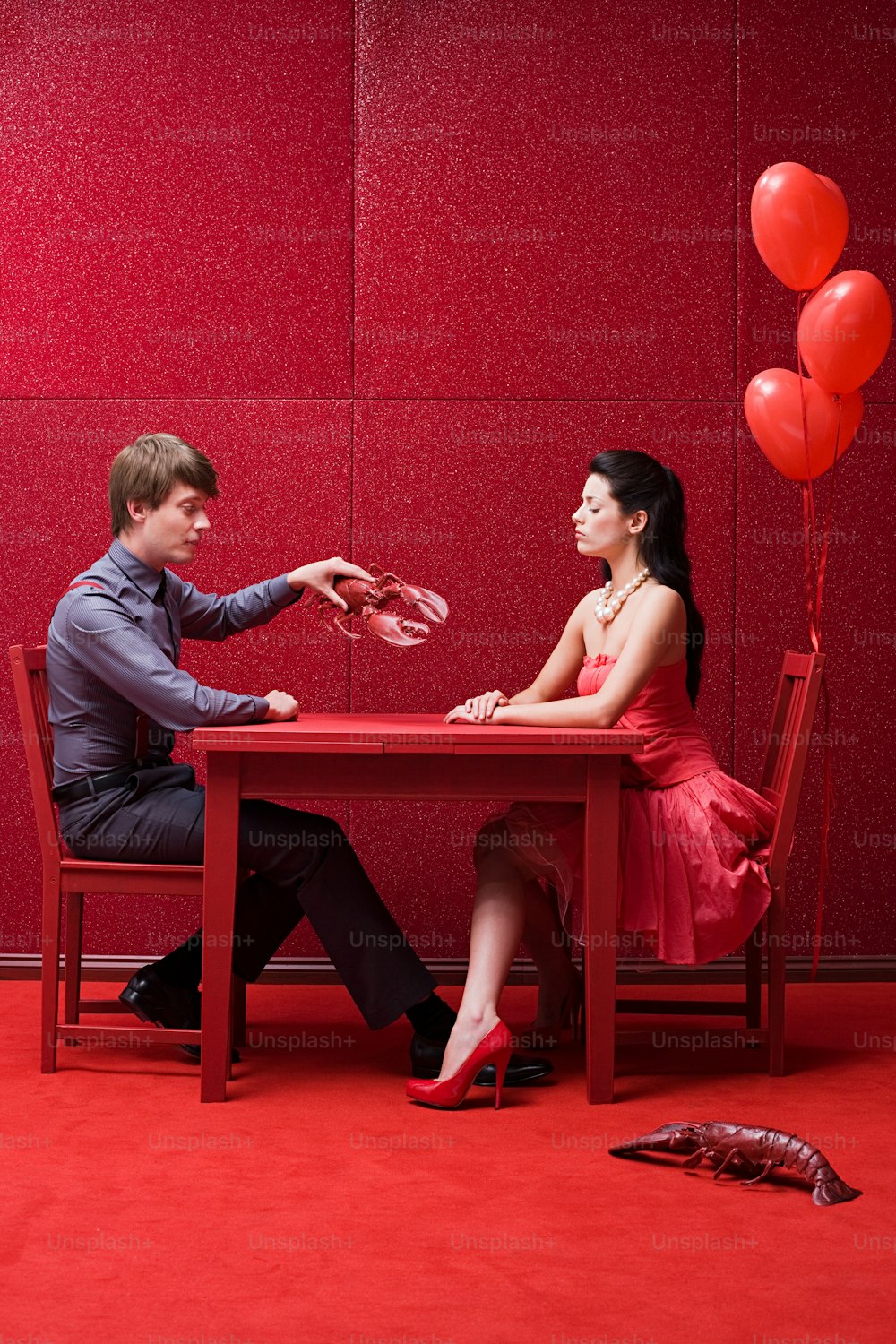 a man and woman sitting at a table with red balloons