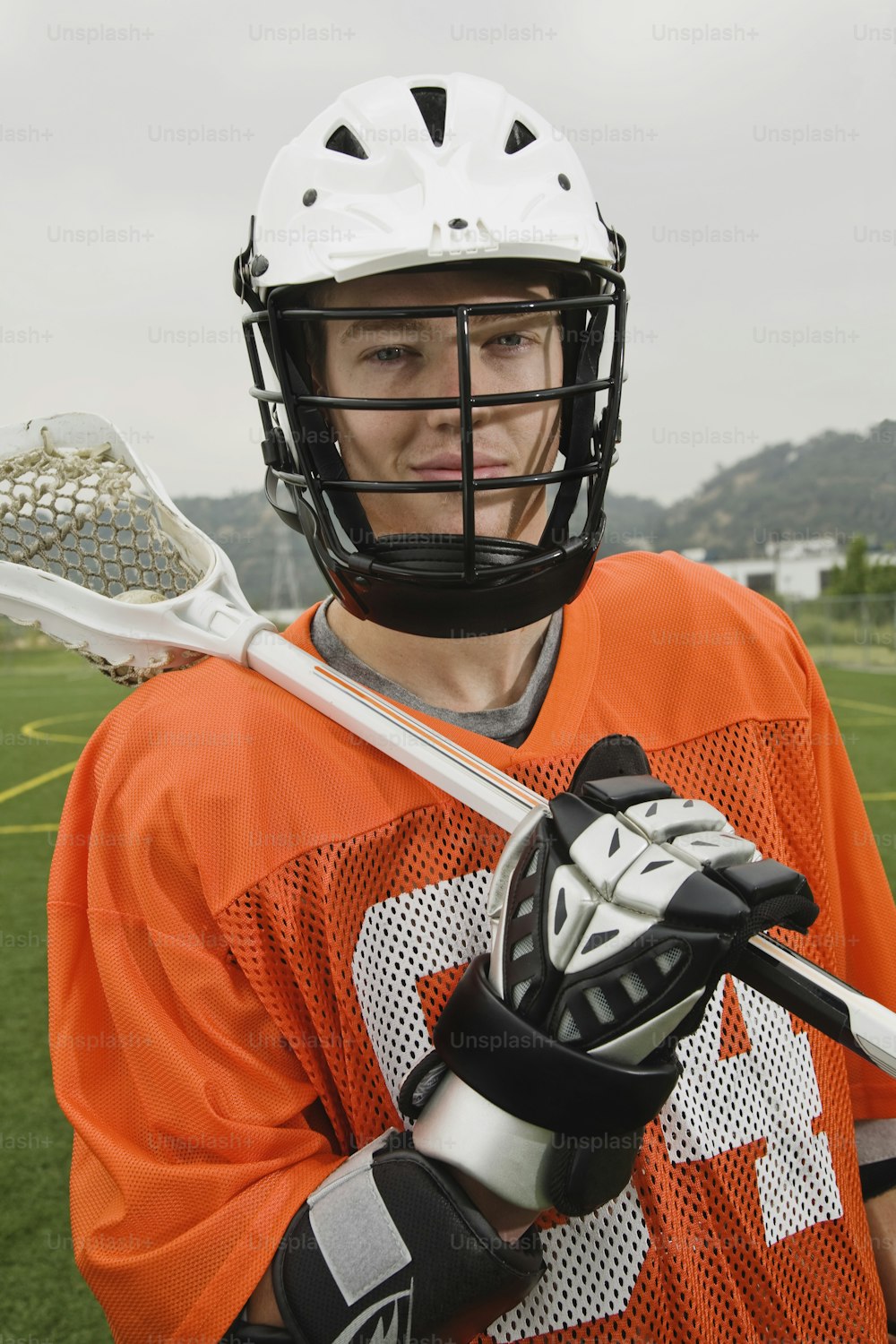 Un hombre con una camiseta naranja sosteniendo un palo de lacrosse