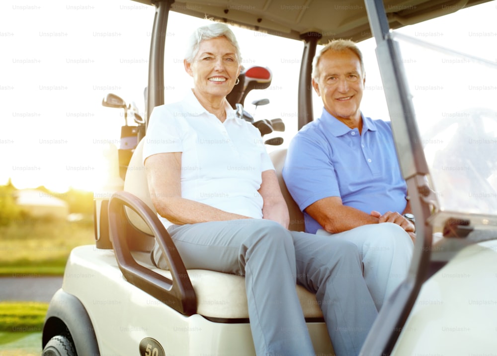 A senior couple sitting in a golf cart on a crisp morning at sunrise