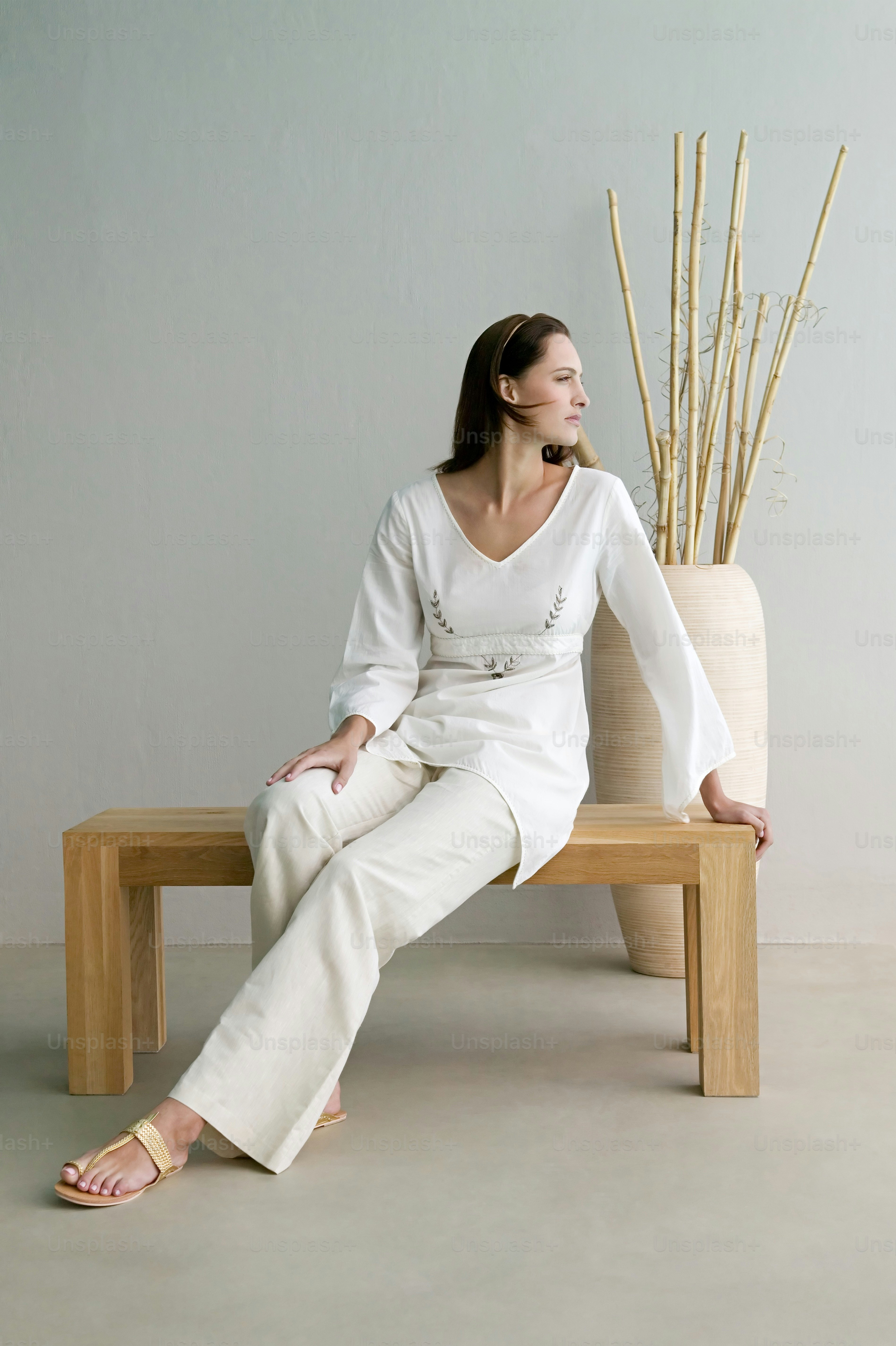 a woman sitting on a wooden bench next to a vase