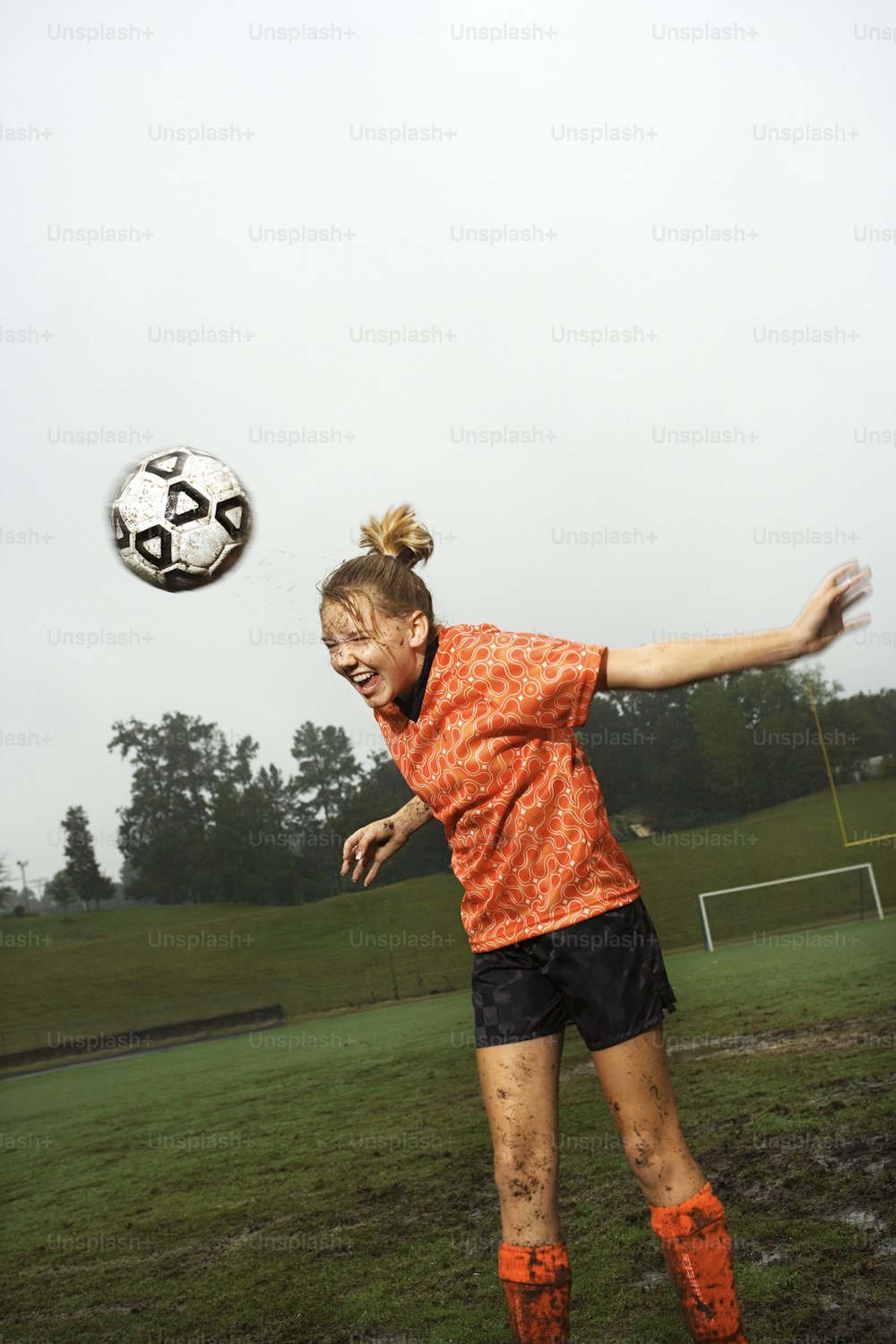 a woman in an orange shirt and black shorts kicking a soccer ball
