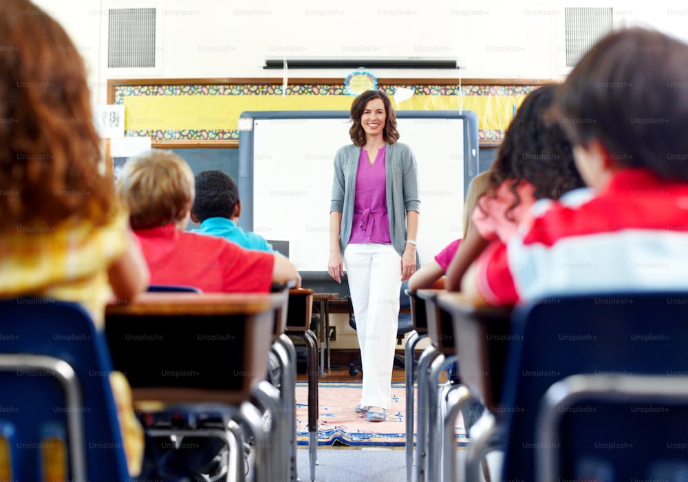 A teacher stands at the front of the class while her seated students look toward her