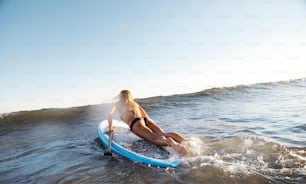A surfer girl jumping onto her paddeboard with paddle in hand