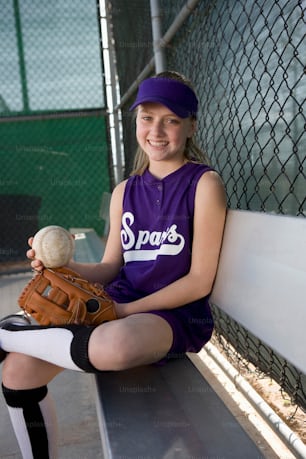a girl sitting on a bench holding a baseball and glove