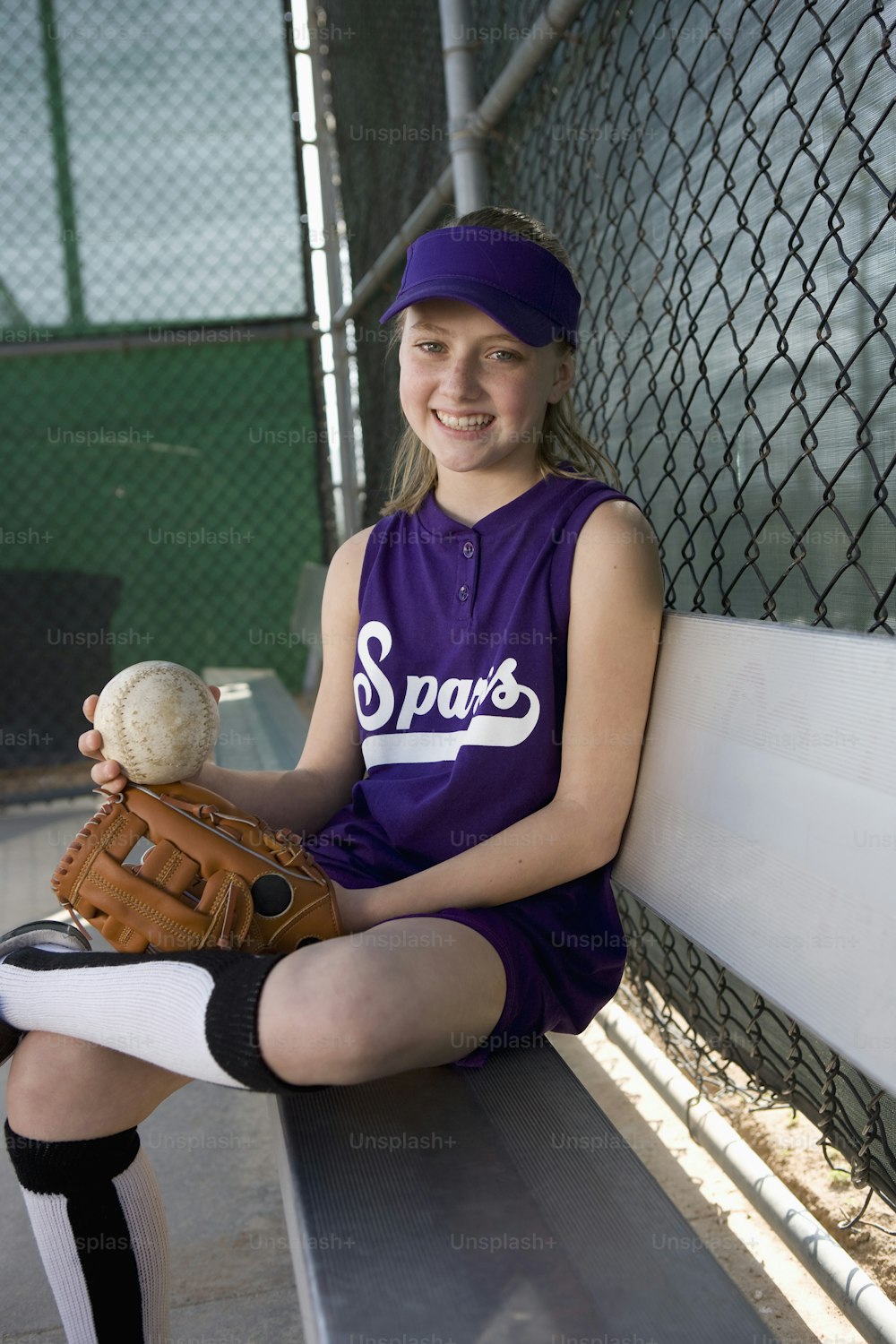 Una niña sentada en un banco sosteniendo una pelota de béisbol y un guante