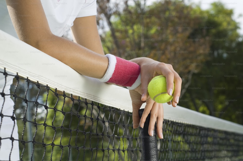 Una mujer sosteniendo una pelota de tenis y una raqueta en una cancha de tenis