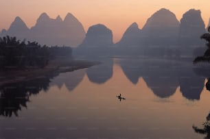 Eine Person in einem kleinen Boot auf einem Fluss mit Bergen im Hintergrund
