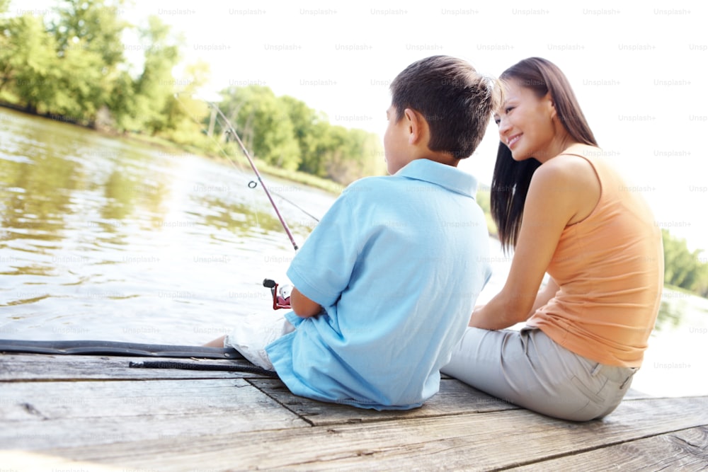 Eine Mutter und ihr Sohn angeln an einem hellen Sommertag von einem Holzsteg
