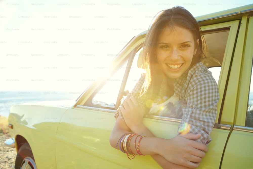 海の景色を見下ろす駐車した車に座っている笑顔の若い女性