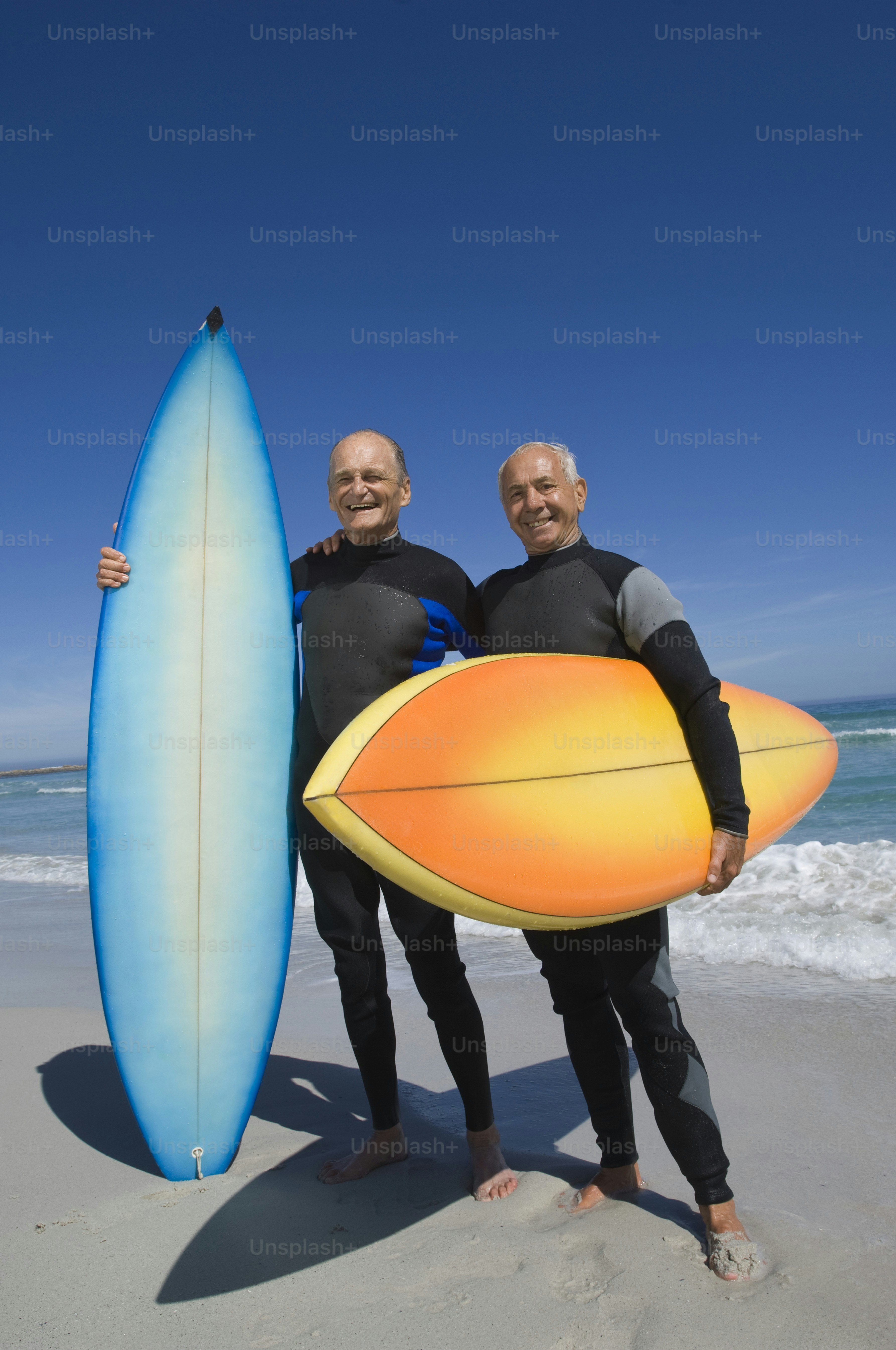 A couple of men standing next to each other on a beach photo – Beach ...