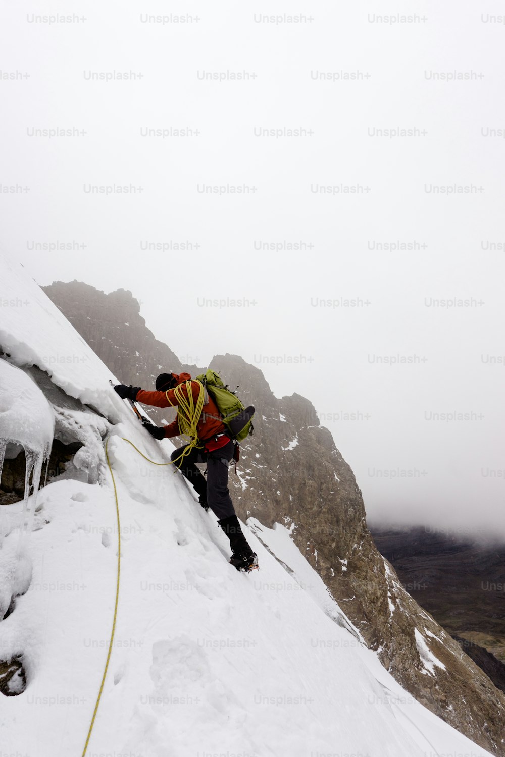 Alpinista maschio in una giacca rossa che scala un ghiacciaio ripido e pericoloso nella Cordillera Blanca nelle Ande in Perù