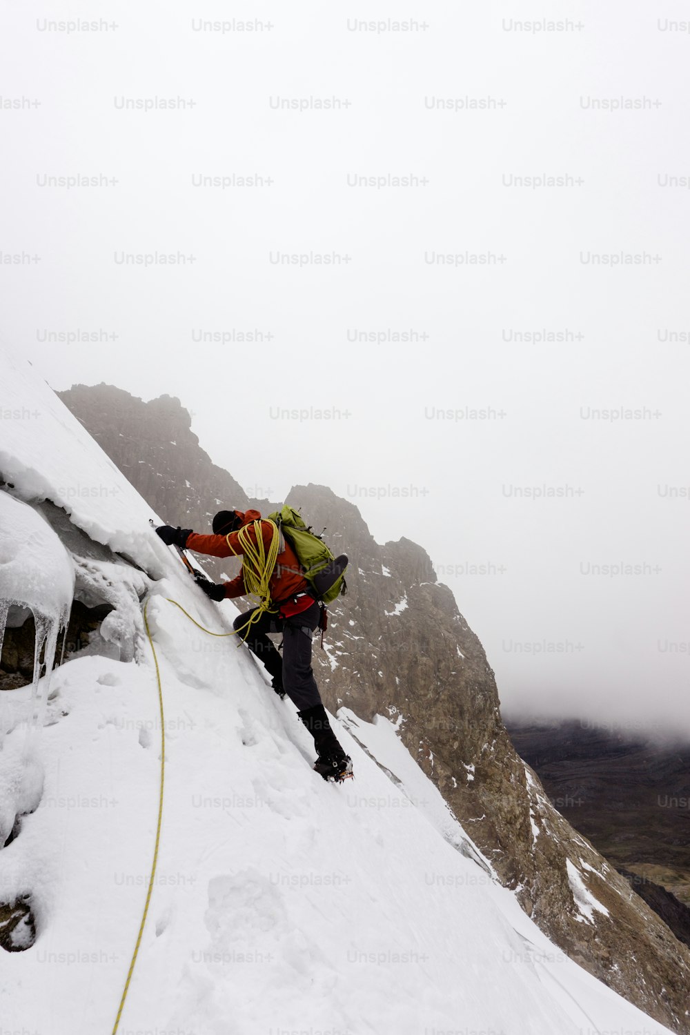 Male mountain climber in a red jacket climbing a steep and dangerous glacier in the Cordillera Blanca in the Andes in Peru