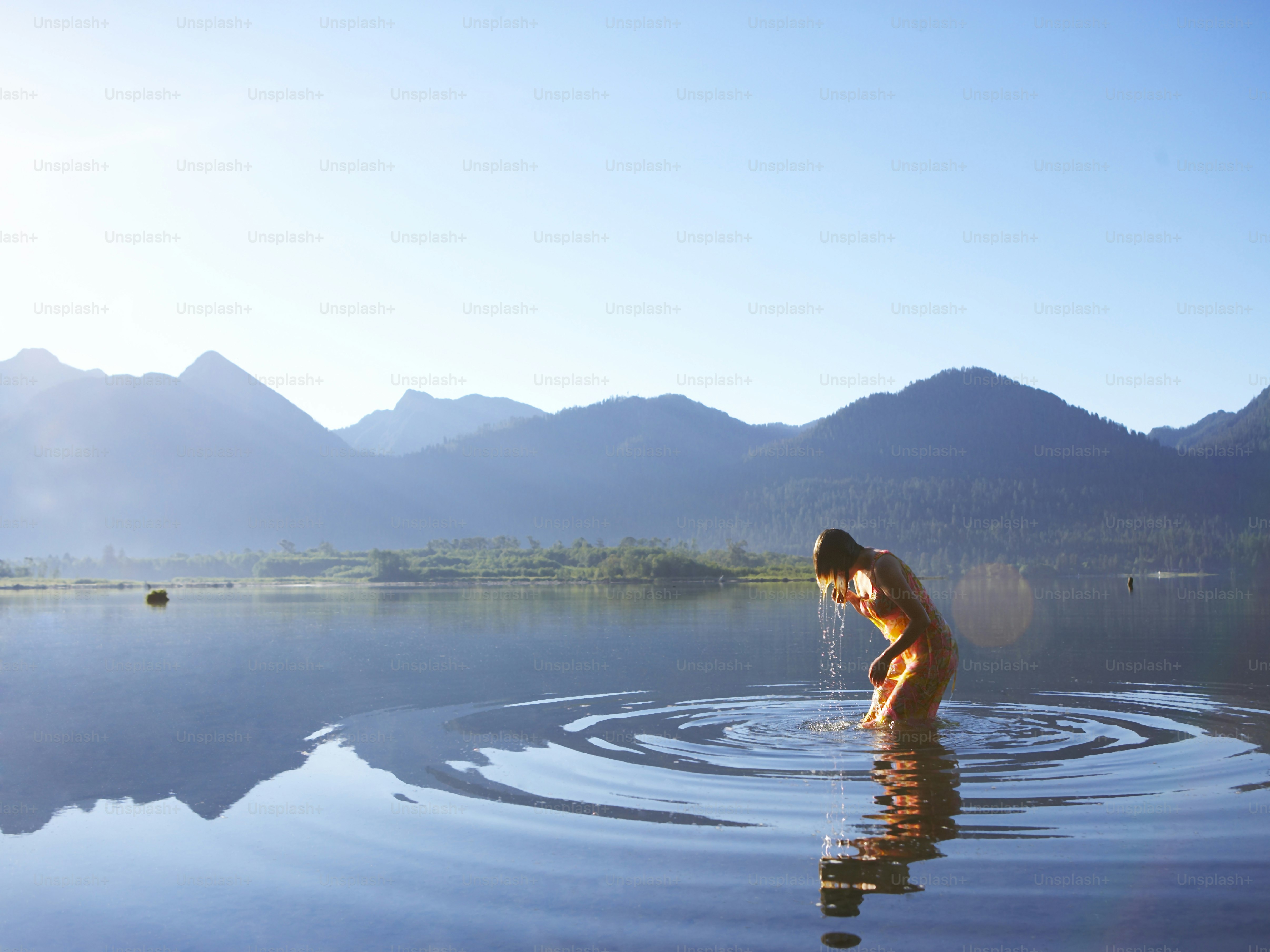 a woman standing in a lake with mountains in the background