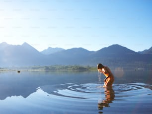 a woman standing in a lake with mountains in the background