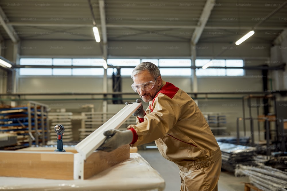Artigiano adulto medio che analizza la tavola di legno lavorata mentre lavora in un laboratorio di falegnameria.